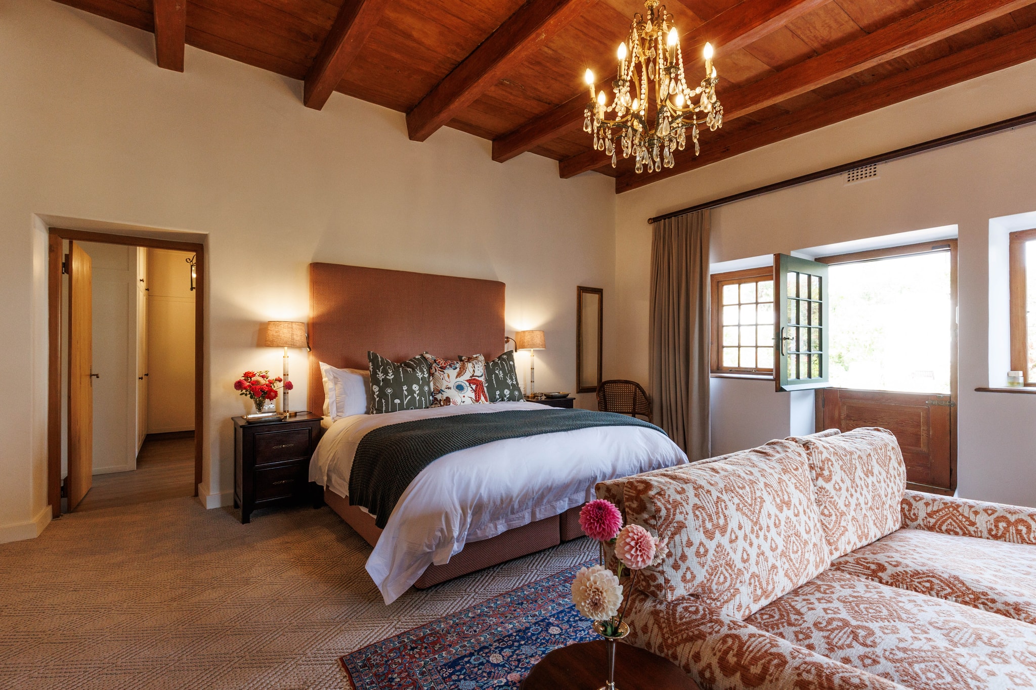 Master bedroom with chandelier, patterned sofa, and pink roses