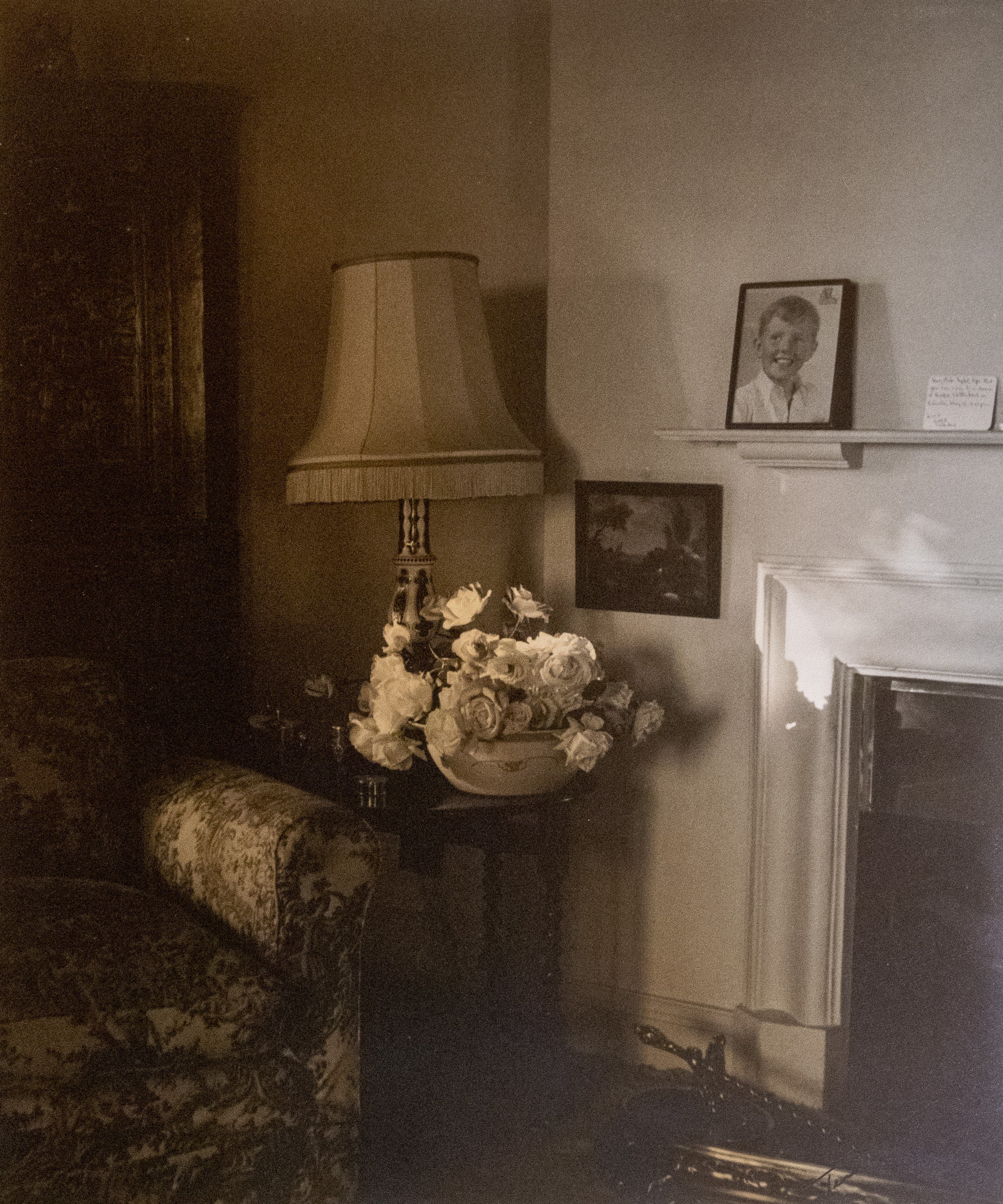 Sepia-toned vintage interior with lamp, roses, and framed portrait by the fireplace