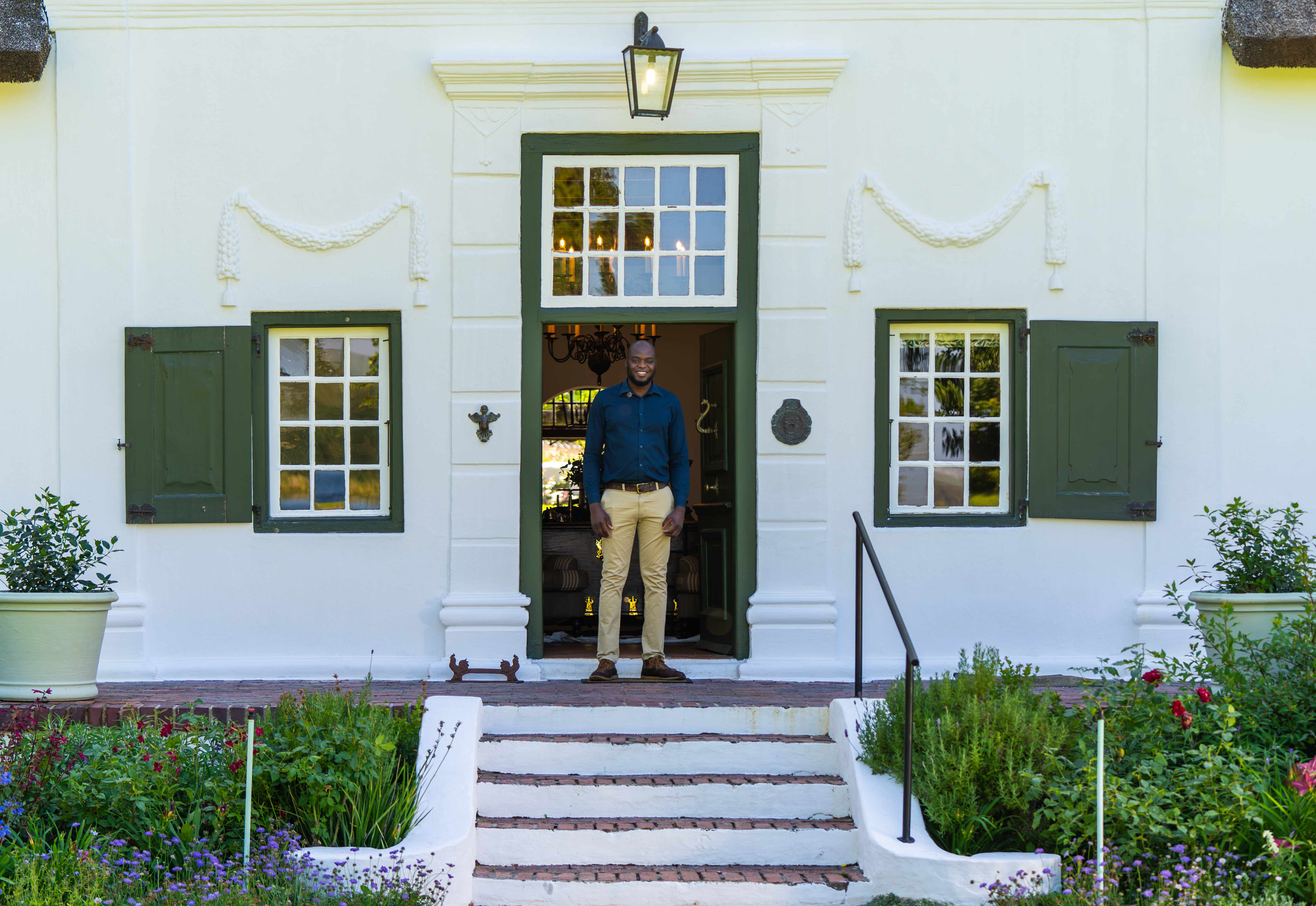 Man standing in the Cape Dutch manor doorway with green shutters and garden steps